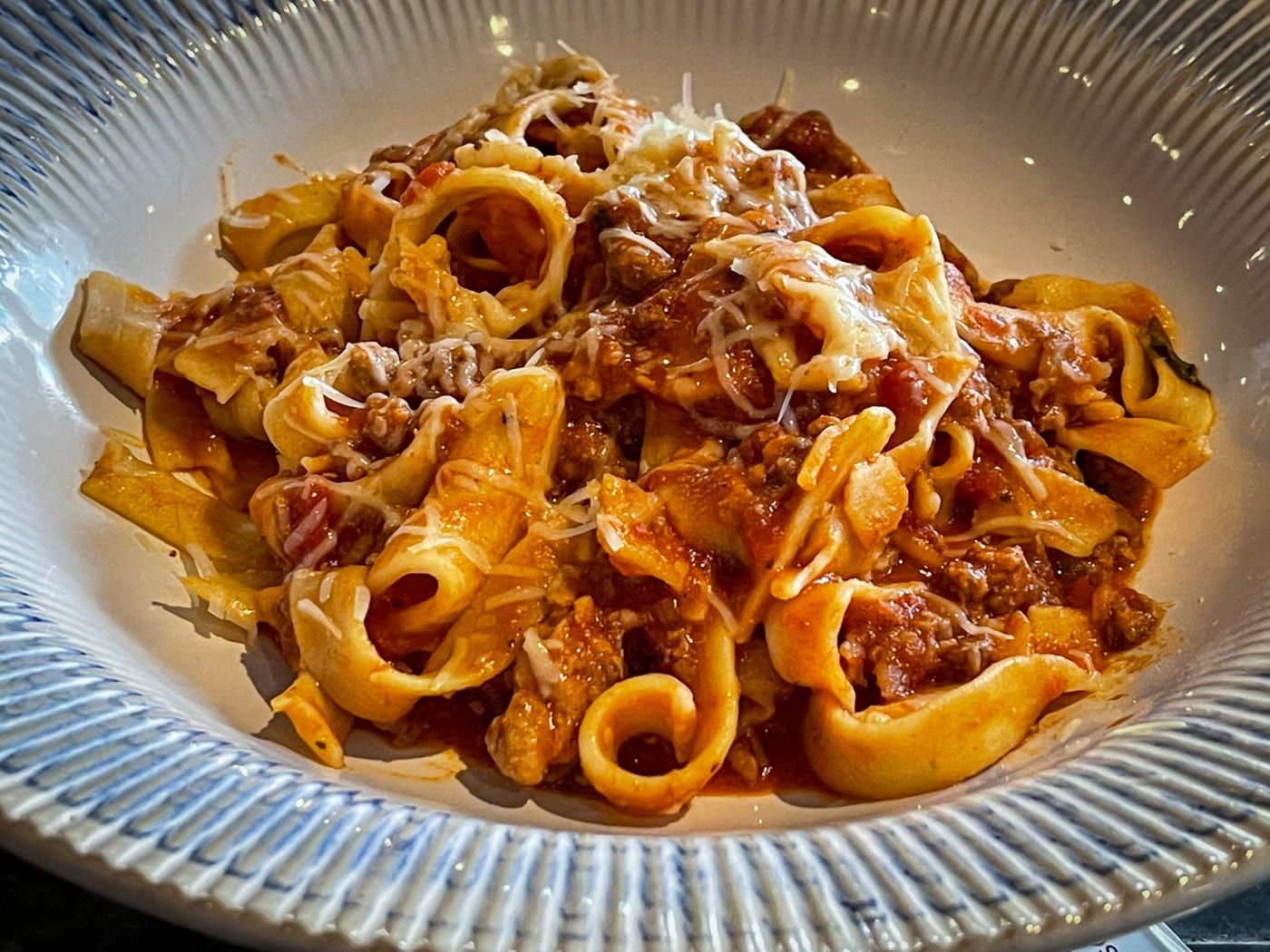 A bowl of fresh pasta in a rich meat sauce, topped with grated cheese
