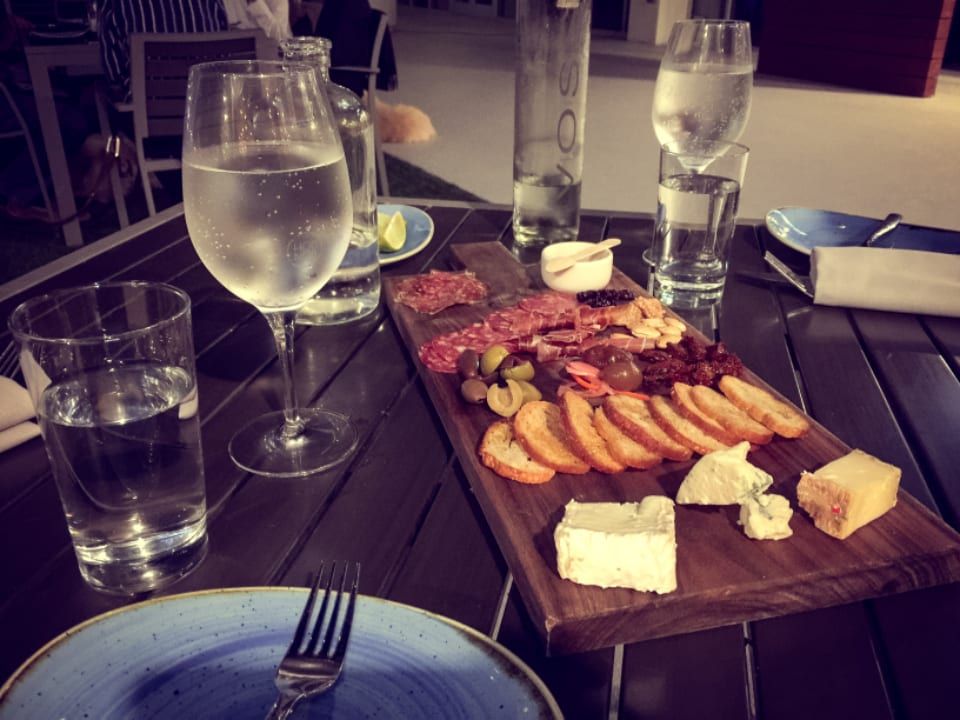 A wooden board of cured meats and cheese beside glasses of white wine