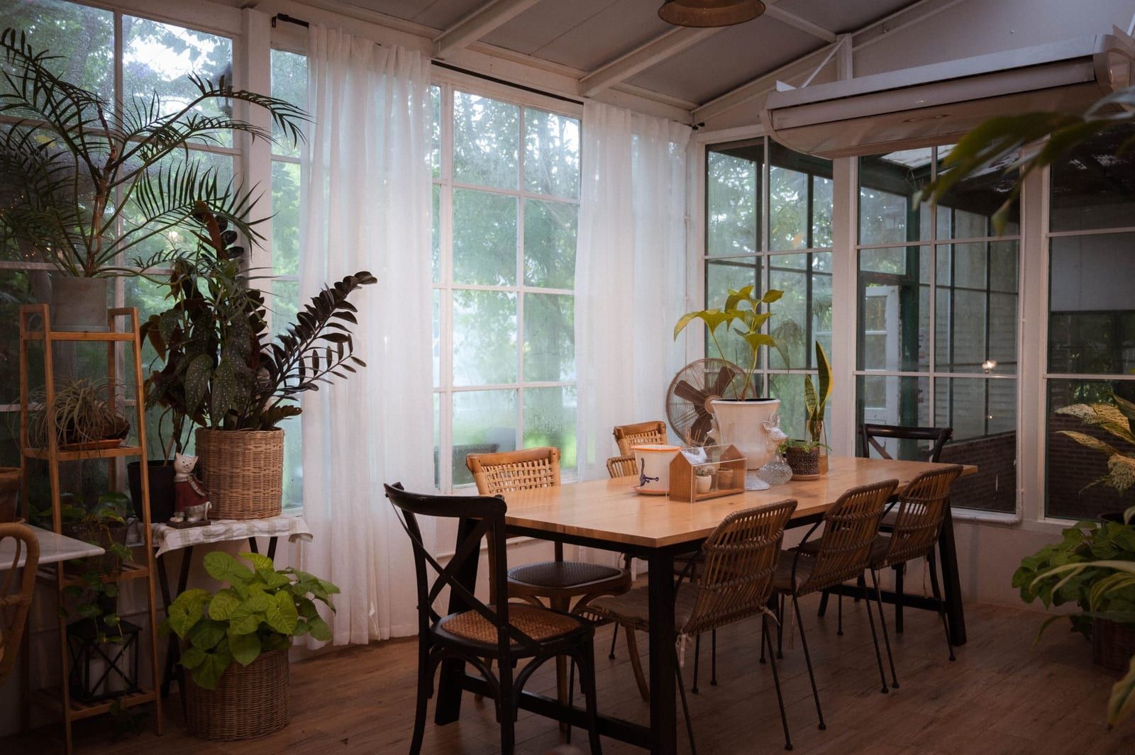 A bright dining room with wooden tables, tall windows and potted plants
