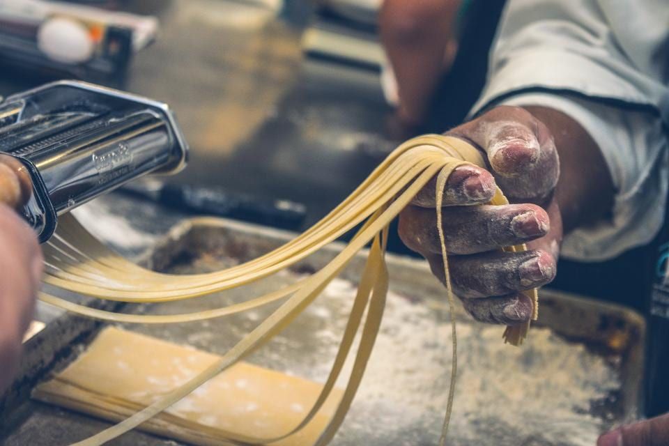 Hands pulling long strands of fresh pasta over a floured board